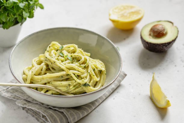Pasta with avocado and Greek basil sauce in a ceramic bowl on a white table